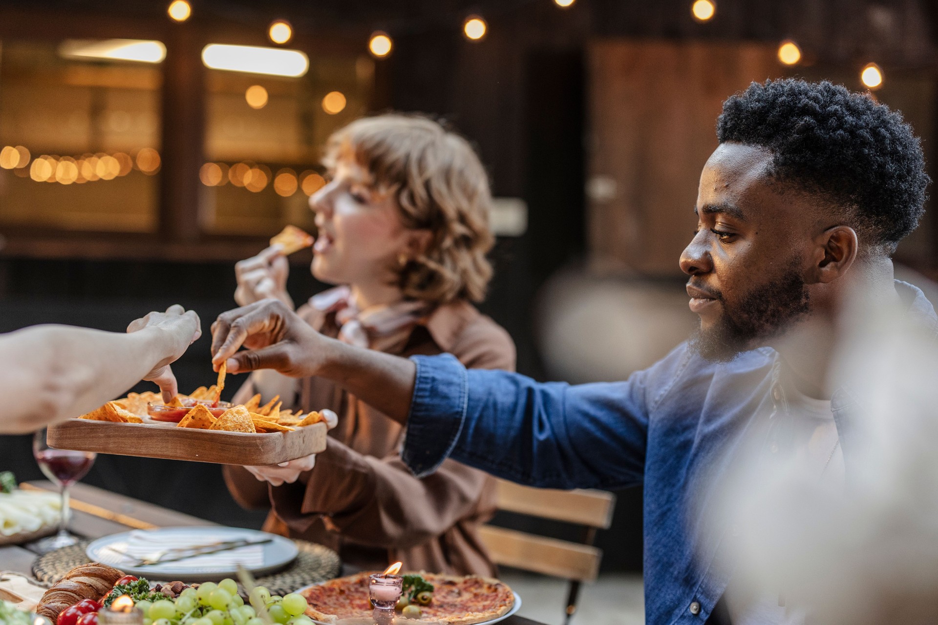 Friends eating nachos and pizza at a multiracial party outdoors